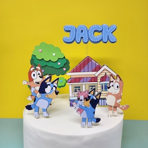Puede incluir: Un juego de adornos para tartas azul y blanco con personajes de la serie animada Bluey. El juego incluye una casa, un &aacute;rbol y cuatro personajes. Los personajes son un perro azul heeler, un perro rojo heeler, un perro rosa heeler y un perro marr&oacute;n heeler. El juego de adornos para tartas es perfecto para una fiesta de cumplea&ntilde;os con tem&aacute;tica de Bluey. El nombre "JACK" est&aacute; escrito en letras azules en la parte superior de la tarta.