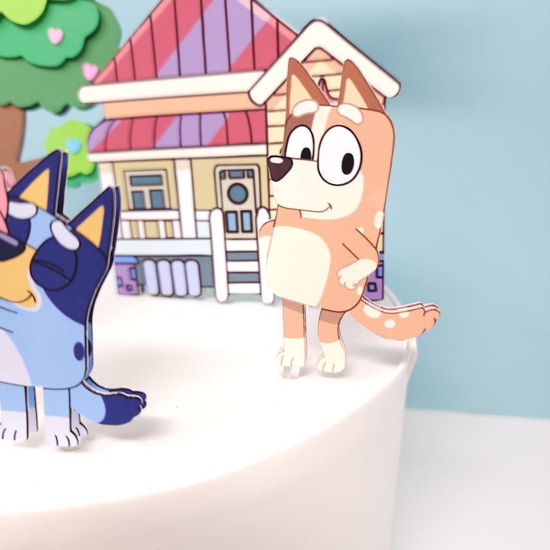 May include: A set of cake toppers featuring a cartoon house, a tree, and two dogs. The house is red and white with a brown roof. The tree is green with pink hearts. The dogs are brown and blue with white spots. The toppers are perfect for a birthday cake or other special occasion.