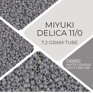 Puede incluir: Primer plano de una colección de pequeñas cuentas cilíndricas de color gris claro. Las cuentas están etiquetadas como "MIYUKI DELICA 11/0" y "7.2 GRAM TUBE". También es visible el código de producto "DB882 MATTE OPAQUE LIGHT GREY AB".
