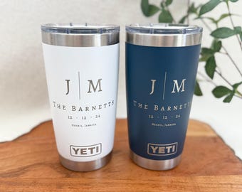 May include: Two personalized YETI tumblers with a white and blue color scheme. The tumblers feature the initials "JM" and the text "THE BARNETTS 12.12.24 NEGRIL, JAMAICA".