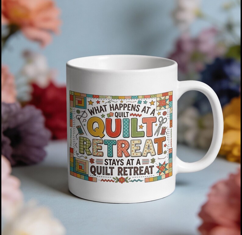 May include: White ceramic mug with the text "WHAT HAPPENS AT A QUILT RETREAT STAYS AT A QUILT RETREAT" in colorful letters and quilt-themed graphics. The mug has a curved handle and is surrounded by blurred floral elements.