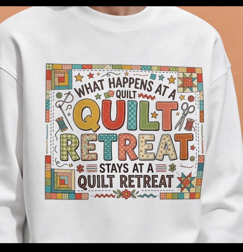 May include: White sweatshirt with a colorful graphic that reads "WHAT HAPPENS AT A QUILT RETREAT STAYS AT A QUILT RETREAT." The design includes images of sewing tools, stars, and quilt block patterns. The sweatshirt is a crew neck style.
