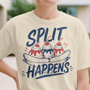 Può includere: T-shirt color crema con grafica di banana split con tre palline di gelato, ciliegie e la scritta "SPLIT HAPPENS" in blu. Il design è di ispirazione vintage.