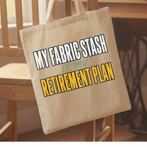 Può includere: Una borsa tote in tela beige con il testo MY FABRIC STASH IS MY RETIREMENT PLAN stampato in lettere maiuscole blu scuro, verdi e gialle. La borsa è dotata di due manici in tessuto e ha una semplice forma rettangolare.