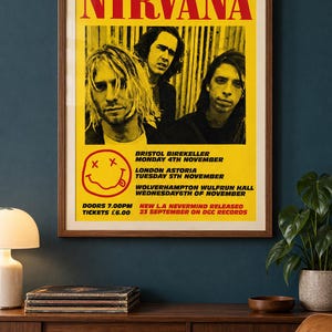 May include: A framed poster featuring a yellow background with the text 1991 U.K. TOUR NIRVANA in red and black. It displays a black and white photograph of three band members, a red smiley face graphic, and tour dates for Bristol, London, and Wolverhampton.