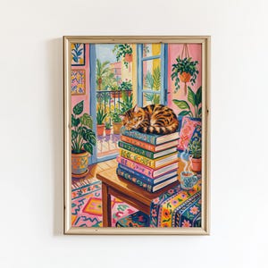 Può includere: Una stampa artistica incorniciata raffigura un'accogliente scena d'interni. Un gatto tigrato dorme sopra una pila di libri colorati su un tavolo di legno. La stanza presenta un balcone con piante, un tappeto fantasia e una tazza di caffè.