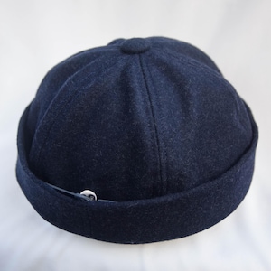 Peut inclure: Un bonnet en laine bleu foncé avec une sangle noire et un bouton argenté.