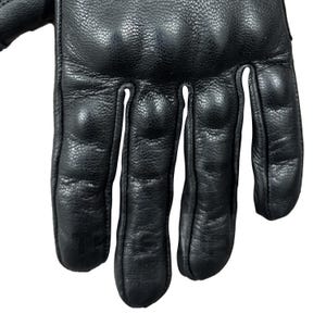 Peut inclure: Gros plan sur un gant en cuir noir. Le gant pr&eacute;sente des sections rembourr&eacute;es sur les jointures et les doigts. Le cuir semble textur&eacute;. Le gant est con&ccedil;u pour la protection et la durabilit&eacute;.