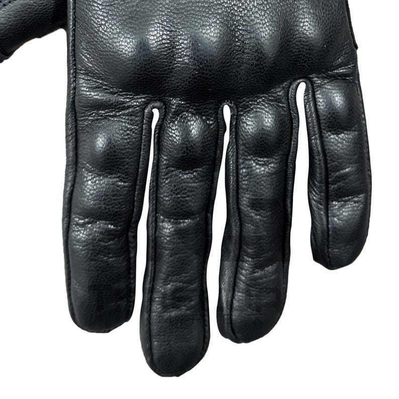 Peut inclure: Gros plan sur un gant en cuir noir. Le gant pr&eacute;sente des sections rembourr&eacute;es sur les jointures et les doigts. Le cuir semble textur&eacute;. Le gant est con&ccedil;u pour la protection et la durabilit&eacute;.