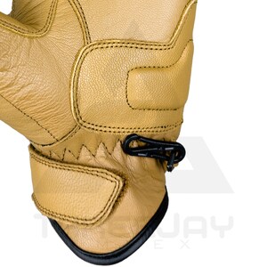 Peut inclure: Gros plan sur un gant de travail en cuir beige avec des d&eacute;tails noirs. Le gant pr&eacute;sente des coutures renforc&eacute;es, une sangle de poignet et un mousqueton noir. Le design sugg&egrave;re durabilit&eacute; et protection.