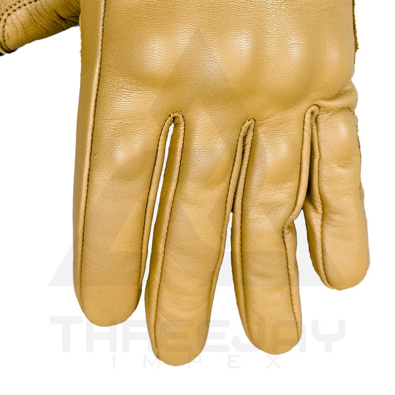 Peut inclure: Gros plan sur un gant en cuir beige. Le gant est en cuir lisse et pr&eacute;sente des coutures visibles le long des coutures. Les doigts sont l&eacute;g&egrave;rement incurv&eacute;s, sugg&eacute;rant un ajustement naturel. Le texte "THREE JOY IMPEX" est visible en bas.