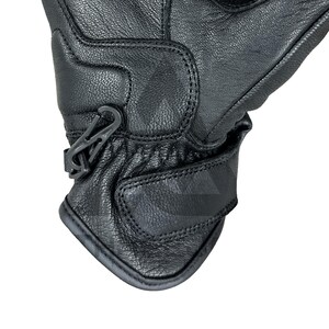 Peut inclure: Gros plan d'un gant en cuir noir avec une surface textur&eacute;e. Le gant pr&eacute;sente des coutures d&eacute;taill&eacute;es et un clip en plastique gris. Une sangle Velcro est pr&eacute;sente au poignet pour l'ajustement. Le gant est con&ccedil;u pour la protection.