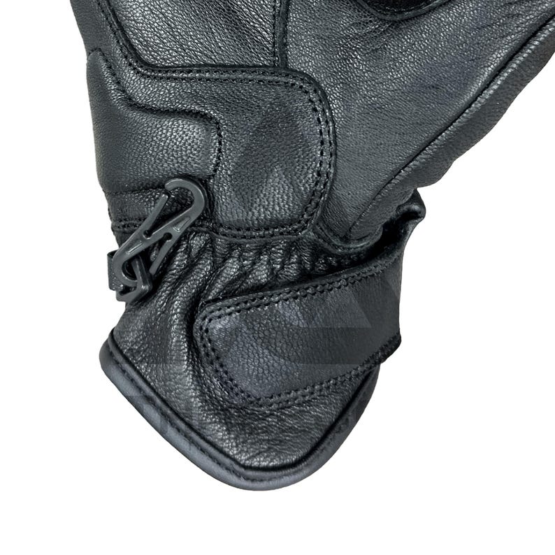 Peut inclure: Gros plan d'un gant en cuir noir avec une surface textur&eacute;e. Le gant pr&eacute;sente des coutures d&eacute;taill&eacute;es et un clip en plastique gris. Une sangle Velcro est pr&eacute;sente au poignet pour l'ajustement. Le gant est con&ccedil;u pour la protection.