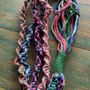 May include: A close-up of a braided rope made of pink, green, blue, and grey cotton. The rope is twisted and knotted, creating a unique and decorative design.