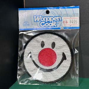 May include: A white iron-on patch with a smiling face and a red nose. The patch is packaged in a clear plastic bag with a blue and white label that reads "Wappen Cook" and "¥495".