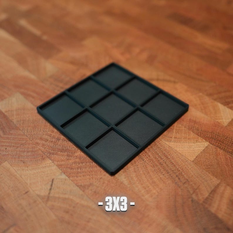 K&ouml;nnte beinhalten: Ein quadratischer, dunkel t&uuml;rkisfarbener Organizer mit neun gleich gro&szlig;en F&auml;chern. Das Produkt ist mit dem Text "-3X3-" in Wei&szlig; beschriftet. Der Organizer liegt auf einer Holzoberfl&auml;che.