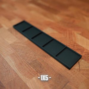 K&ouml;nnte beinhalten: Ein schwarzer rechteckiger Tablett mit vier gleich gro&szlig;en F&auml;chern. Das Tablett besteht aus einem matten Material und ist vor einem Holzgrund platziert. Der Text "-1X5-" befindet sich unten.