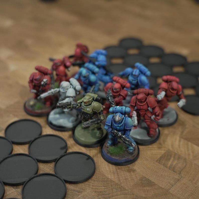 Pode incluir: Miniaturas de soldados em armaduras vermelhas, azuis, verdes e cinzentas, com armas. As miniaturas est&atilde;o em pequenas bases redondas, dispostas sobre uma superf&iacute;cie de madeira. V&aacute;rias bases redondas pretas tamb&eacute;m s&atilde;o vis&iacute;veis.