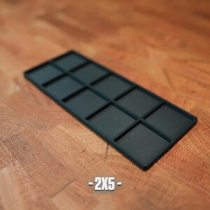K&ouml;nnte beinhalten: Ein dunkelblaugr&uuml;nes rechteckiges Tablett mit zehn quadratischen F&auml;chern. Das Tablett befindet sich auf einer Holzoberfl&auml;che. Der Text "-2X5-" ist unten im Bild in Wei&szlig; gedruckt. Das Tablett wird wahrscheinlich zum Ordnen kleiner Gegenst&auml;nde verwendet.