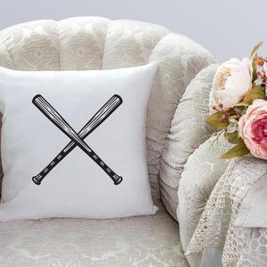 May include: White throw pillow with a black graphic of two baseball bats crossed over each other.