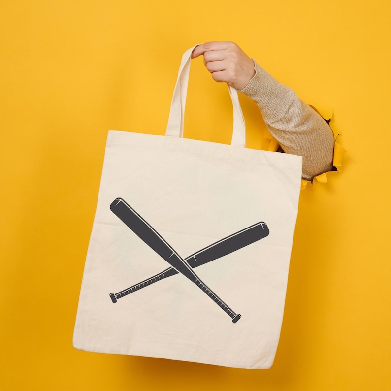 May include: A white tote bag with a black baseball bat design. The bag is held by a hand reaching through a yellow background.