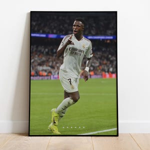 Puede incluir: Un jugador de fútbol con una camiseta blanca con el texto "Emirates Fly Better" en la parte delantera, corre por un campo verde. El jugador lleva pantalones cortos negros y tacos amarillos.