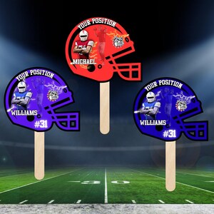 May include: Three football helmet-shaped fan props in red and blue, each with a wooden handle. The props feature player images, names, and the text "YOUR POSITION." One prop reads "MICHAEL," and two read "WILLIAMS #31."