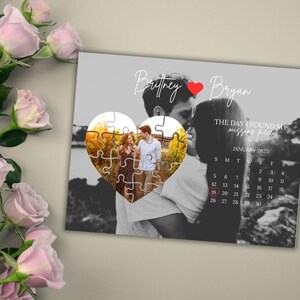May include: A personalized heart-shaped puzzle with a couple's photo, set against a grayscale background. The puzzle is surrounded by a calendar for January 2025, with the date circled. The names "Britney" and "Bryan" are written above the puzzle.