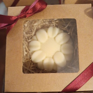Könnte beinhalten: Eine weiße, blumenförmige Seife in einer braunen Pappbox mit rotem Band. Die Seife liegt in zerkleinertem Papier.