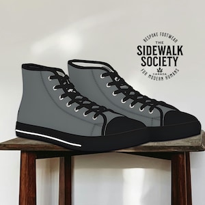May include: A pair of gray high-top sneakers with black laces and a white sole. The shoes are on a wooden table. The text on the label reads "Bespoke Footwear The Sidewalk Society For Modern Humans Canada"