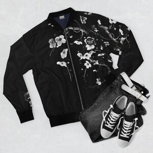 May include: Black bomber jacket featuring a white floral pattern and the text "Subconscious Surfer". The jacket is displayed with dark denim jeans, a white belt, and black and white trainers.