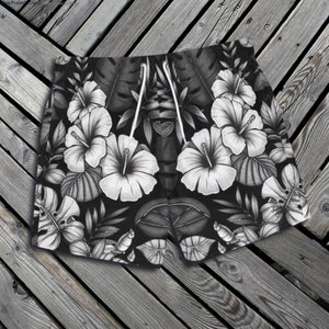 Puede incluir: Bañador de hombre con estampado de flores tropicales en blanco y negro. El estampado presenta flores de hibisco, hojas y otras plantas tropicales.