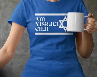 May include: A royal blue t-shirt with the text "Am Yisrael Chai" in white, along with a white Star of David. A white mug is held in the hand. The shirt is a short-sleeved crew neck.