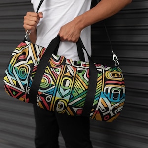 May include: A patterned duffel bag featuring a vibrant geometric design in yellow, green, blue, red, and black. It has black handles and a shoulder strap. The bag is cylindrical and made of fabric.