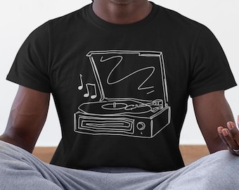 Puede incluir: Una camiseta negra con un contorno blanco de un tocadiscos vintage con un disco en el plato giratorio y notas musicales que salen del altavoz.