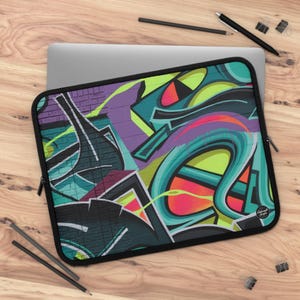 Peut inclure: Une housse d'ordinateur portable avec un motif graffiti coloré comprenant des couleurs vertes, bleues, violettes, jaunes et rouges. Le motif est abstrait et présente une variété de formes et de lignes.