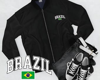 May include: Black bomber jacket with "BRAZIL" text and a Brazilian flag graphic. The jacket is paired with dark wash jeans, a white belt, and black and white trainers. The overall theme is casual wear.