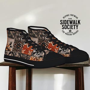May include: A pair of high-top canvas shoes with a black sole and a colourful patterned design. The shoes feature a patchwork design with floral and geometric motifs in shades of orange, brown, and white. The shoes are sitting on a wooden surface. The text "The Sidewalk Society" is printed on a circular tag attached to the shoes.