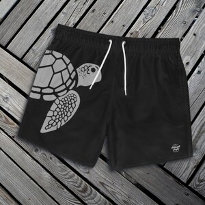May include: Black swim trunks with a white silhouette of a sea turtle on the left leg. The trunks have a drawstring waist and a small logo on the right leg.