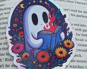Könnte beinhalten: Holografischer Aufkleber mit einem Geist, der ein Buch liest, umgeben von Blumen und Himmelselementen. Das Design zeigt einen freundlichen Geist mit Flammen aus dem Buch. Ein skurriler Aufkleber.