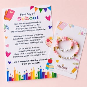 May include: Two beaded bracelets on a display card featuring the names EMILY and MOMMY, accompanied by a printed poem titled First Day of School. The card displays colorful illustrations of pencils, notebooks, and hearts on a white background.