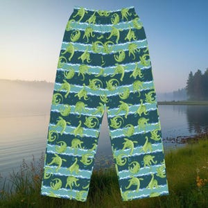 Könnte beinhalten: Grüne und blaue Schlafanzughose mit einem sich wiederholenden Muster aus grünen Meereskreaturen. Die Hose hat ein gestreiftes Design mit horizontalen Linien in verschiedenen Blau- und Grüntönen. Die Schlafanzughose ist aus einem weichen, bequemen Material.