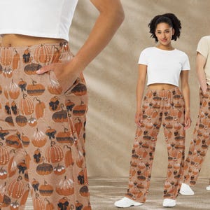 May include: Tan pajama pants with a repeating pattern of orange, brown, and black pumpkins. The pants have a relaxed fit and pockets. The image shows the pants on three people, suggesting a fall or Halloween theme.