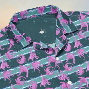 Könnte beinhalten: Ein Hemd mit Knöpfen und einem sich wiederholenden Muster aus rosa Meereskreaturen auf einem türkis-weiß gestreiften Hintergrund. Das Hemd hat einen Kragen und weiße Knöpfe. Das Design ist skurril und auffällig.