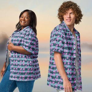 May include: Two people wearing matching short-sleeved button-down shirts. The shirts feature a repeating pattern of pink figures on a dark teal background with horizontal stripes of light teal. The shirts are paired with blue jeans.