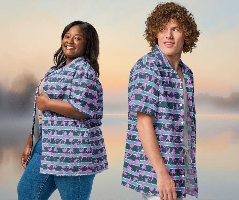 May include: Two people wearing matching short-sleeved button-down shirts. The shirts feature a repeating pattern of pink figures on a dark teal background with horizontal stripes of light teal. The shirts are paired with blue jeans.