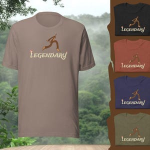 Könnte beinhalten: Ein hellbraunes T-Shirt mit dem Wort "Legendary" in einer stilisierten Schriftart und einer Cartoonfigur. Zusätzliche Shirts in Schwarz, Rost, Marineblau und Olivgrün werden rechts angezeigt.