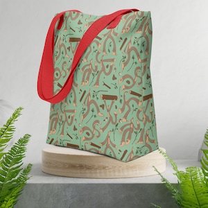 Könnte beinhalten: Eine grüne Einkaufstasche mit einem braunen und beigefarbenen Muster aus abstrakten Formen und Linien. Die Tasche hat rote Henkel.
