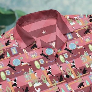 May include: A button-down shirt with a camp collar featuring a repeating pattern of black and white cats, shelves, plants, and framed pictures on a pink and maroon striped background. The shirt has black buttons and a geometric design.