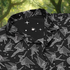 May include: Black button-up shirt with a repeating pattern of stylized figures, geometric shapes, and stars. The collar features a contrasting black fabric with a celestial design. The shirt's design is a unique and artistic statement.